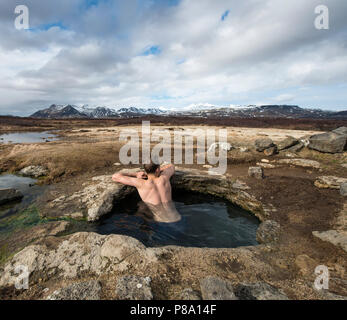 Jeune homme dans une source thermale, près de l'Eyjar og Miklaholt, Vesturland, Islande Banque D'Images