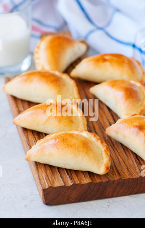 De pommes de terre maison empanadas farcies sur une planche de bois. Arrière-plan de pierre blanche. Banque D'Images