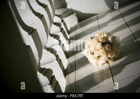 Une scène poétique d'un beau bouquet de mariée en forme de tour d'ivoire roses sur le sol d'une terrasse à l'ombre d'une pierre blanche classique... Banque D'Images