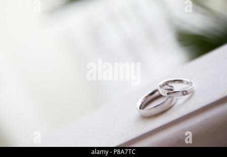 Une belle scène de deux anneaux de mariage en or blanc, posé sur un rebord en bois avec un beau bokeh. La bague de la mariée bejeweled est sur le dessus de la marié... Banque D'Images