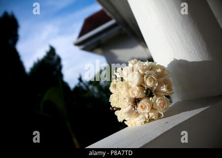 Un beau bouquet de mariée en forme de rond frais d'ivoire roses sur un rebord de balcon d'une maison coloniale tôt le matin. Banque D'Images