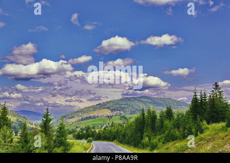 Des nuages dans le ciel bleu au-dessus de la route entre le vert des montagnes des Carpates . Pour votre conception Banque D'Images