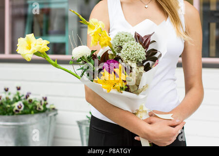 Jeune femme tenant un bouquet de fleurs asymétriques modernes sur la rue près de flower shop Banque D'Images