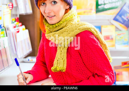 Jeune femme en boutique à l'achat de billets de loterie Banque D'Images
