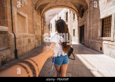 Vue arrière de jeune femme menant personne méconnaissable à la main tout en marchant ensemble sur l'ancienne rue de valence le jour ensoleillé Banque D'Images