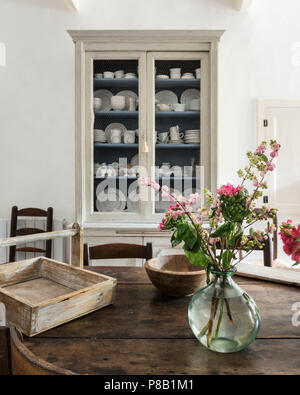 Fleurs roses sur table xixe avec display cabinet d'assiettes et tasses Banque D'Images