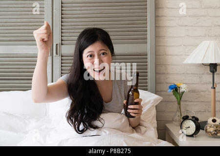 Jeune femme asiatique tenant dans ses mains une bouteille de bière est satisfait de la fin heureuse. L'intrigue est la table. L'acteur est riche d'émotion ses acclamations. Banque D'Images