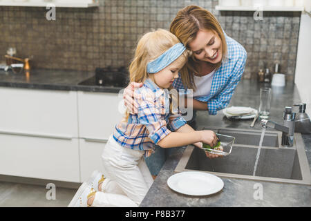 Vue de côté de fille mère aidant à faire la vaisselle après le dîner à la maison Banque D'Images