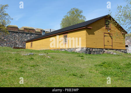 Cabane en bois jaune avec un toit noir et fondations de pierre sur un patch d'herbe sur l'île de Suomenlinna Banque D'Images