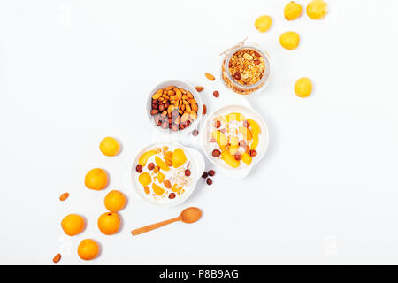 Composition jaune vif avec fruits frais, céréales et noix, vue d'en haut. Deux bols de muesli avec du yaourt, les noisettes et les abricots près de pot et cuillère, f Banque D'Images