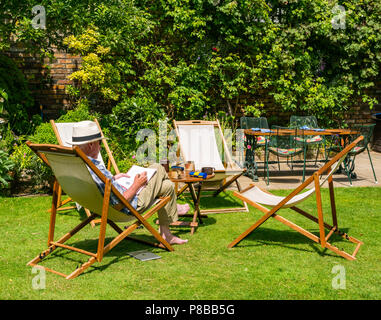 Plus un homme portant chapeau Panama problèmes mots croisés assis dans une chaise dans grand jardin en été, canicule, London, England, UK Banque D'Images