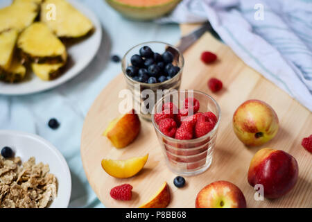 Saine alimentation végétalien végétarien savoureux petit-déjeuner détox avec fruits frais de saison et de baies servi sur planche à découper sur fond bleu pastel Banque D'Images