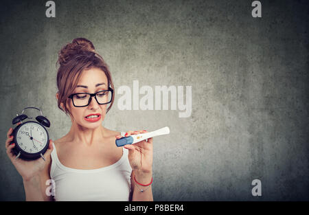 Jeune femme dans les verres holding réveil et le test de grossesse en attente de résultat de l'anxiété Banque D'Images