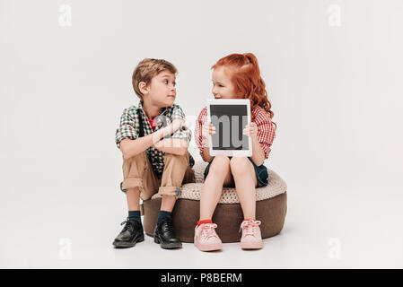 Beaux enfants regardaient et montrant avec tablette numérique écran blanc isolé sur gray Banque D'Images