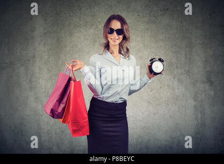 Woman holding shopping bags élégant et réveil montrant de temps pour la vente et des rabais sur fond gris Banque D'Images