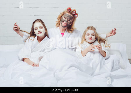 Heureuse mère et filles au lit avec masques visage beauté Banque D'Images