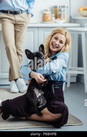 Homme debout par happy woman hugging bouledogue français sur le sol de la cuisine Banque D'Images