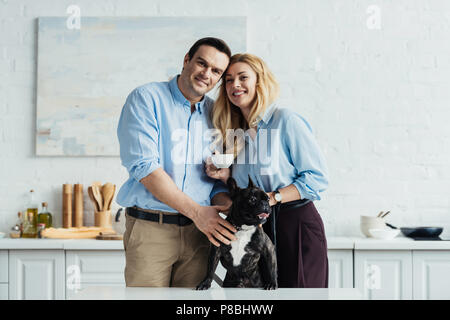 Smiling couple caresser leurs frenchie chien sur une table de cuisine Banque D'Images