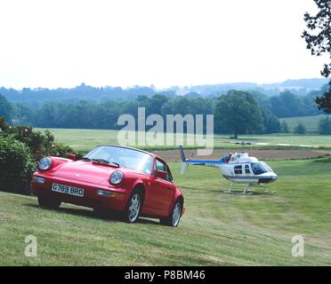 Porsche 911 Carrera 4 - modèle 1990 année en rouge dans un manoir et la campagne avec l'hélicoptère en arrière-plan Banque D'Images