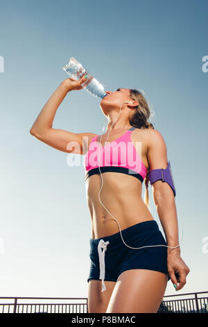 Low angle view of young de la sportive des écouteurs avec le smartphone en exécutant armband case l'eau potable de la bouteille sur le toit Banque D'Images