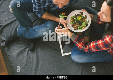 Jeune couple, c'est de se nourrir l'un l'autre et souriant allongé sur le lit le matin Banque D'Images