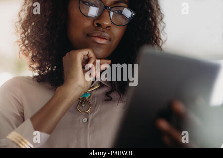 Gros plan d'une femme aux cheveux bouclés en spectacles looking at tablet pc with hand on chin. Low angle view of woman entrepreneur in formal attire l Banque D'Images