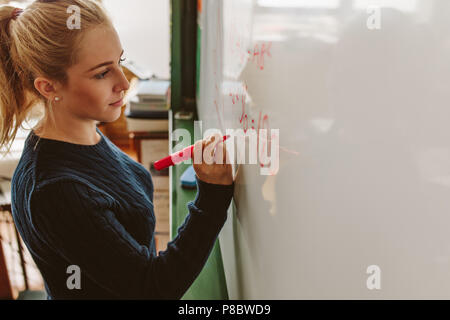 Close up of female student écrit une équation sur un tableau blanc dans la classe. L'écriture de fille à bord pendant les cours de maths. Banque D'Images