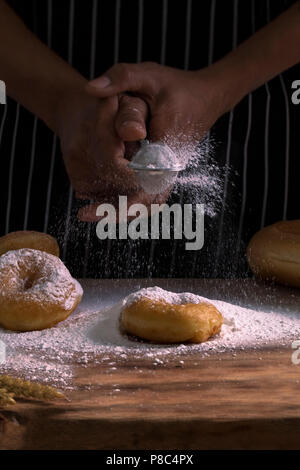 Les mains d' Chef des beignets sucrés saupoudrer de sucre glace et de tamis à farine sur background.Copier l'espace. Banque D'Images