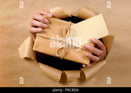 Les mains de l'homme ou la livraison de colis à travers donnant papier fond marron déchiré Banque D'Images