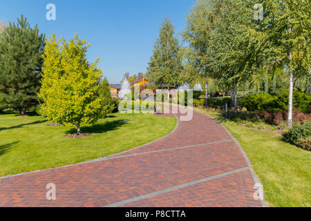 Piste rouge entre la plantation d'arbres et d'herbe verte juteuse, menant à une fontaine près de la maison. Petrivtsi Novi, l'Ukraine . Pour votre conception Banque D'Images