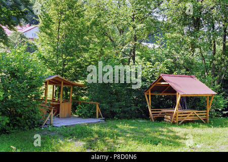 Un abri pour le repos avec des bancs et une table debout dans l'ombre de buissons et d'arbres sur l'herbe verte. Un bon endroit pour se détendre dans la paix et la solitude. Banque D'Images