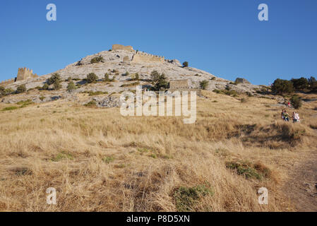 Pente d'une colline recouverte d'herbe sèche avec des restes de murs à créneaux d'une ancienne forteresse contre un ciel bleu et les touristes en ordre décroissant vers le bas le Banque D'Images