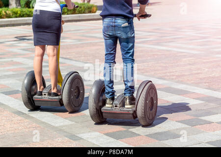 Couple dans les tenues de riding scooter gyro moderne hover board au city street sur journée ensoleillée. Eco transport urbain électrique futur gadget. Banque D'Images