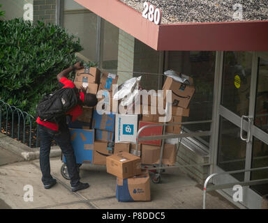 Un livreur de Lasership avec son chariot chargé d'achats de l'aime de Amazon, tablier bleu, et d'autres sortes ses livraisons à un immeuble le quartier de Chelsea, New York, le vendredi 6 juillet 2018 . (Â©Â Richard B. Levine) Banque D'Images