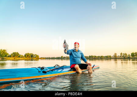 Hauts pagayeur assis sur un stand up paddleboard et rinçage sandales - un lac calme lac calme dans le nord du Colorado, le paysage d'été Banque D'Images