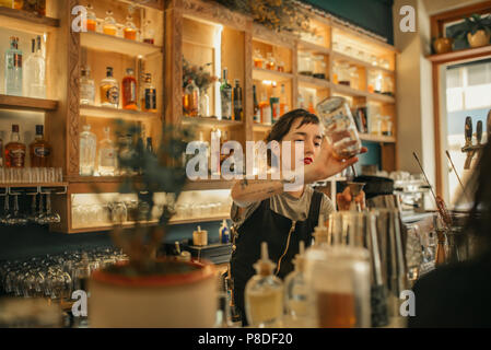 Jeune femme bartender pouring cocktails derrière un comptoir bar Banque D'Images