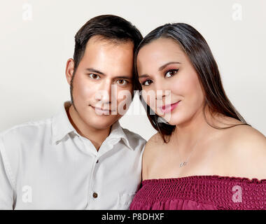 Jolie jeune femme portant une robe sans manches bourgogne debout à côté de son mari qui porte une chemise blanche regardant la caméra et smiling Banque D'Images