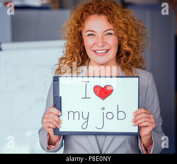 Red haired smiling businesswoman holding petite affiche. Businesswoman heureux avec son travail. Tonique concept. Banque D'Images