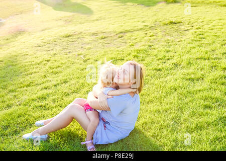 Famille heureuse sur la nature. Maman et bébé fille bébé, détente, rire et s'amuser sur l'herbe verte prairie au coucher du soleil. Passer du temps Banque D'Images