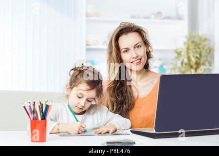 Jeune maman - business woman working on laptop et sa fille de cinq ans s'appuie avec des crayons Banque D'Images