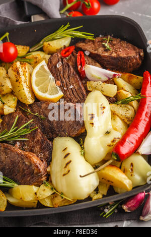 Steaks de boeuf grillée avec des pommes de terre et les légumes dans une poêle grill, macro. Banque D'Images