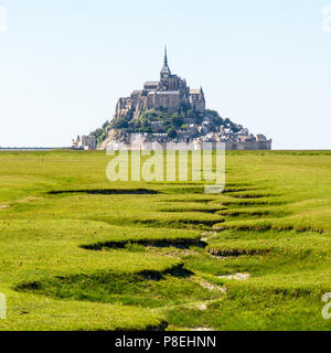 Vue sur le Mont Saint-Michel, l'île de marée en Bretagne, France, avec le lit à sec d'un ruisseau qui serpente dans la prairie de sel au premier plan. Banque D'Images