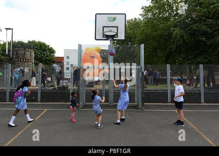 Les enfants jouer au baseball en face de l'Atout Baby Blimp, tandis qu'il est gonflé pendant un test de pratique, à Bingfield Park au nord de Londres. Banque D'Images