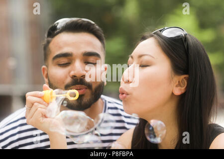 Couple holding a bubble wand soufflant des bulles de savon Banque D'Images