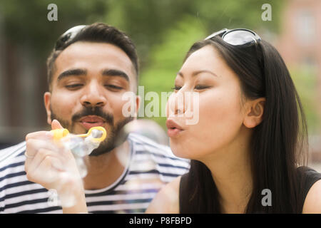 Couple holding a bubble wand soufflant des bulles de savon Banque D'Images