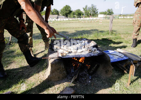 La préparation des soldats repas sur une grille à la main en bois ouverte sur le feu, à un camp de survie. Ils cuisent des serpents d'eau, les poissons, les grenouilles et le pain. Banque D'Images