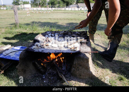 La préparation des soldats repas sur une grille à la main en bois ouverte sur le feu, à un camp de survie. Ils cuisent des serpents d'eau, les poissons, les grenouilles et le pain. Banque D'Images