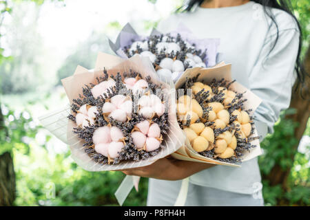 Trois belles et bouquets différents avec lavande en coton femme mains . fleurs couleur lilas. placé dans un sac de papier coloré de fleurs. mélange de couleurs. Banque D'Images