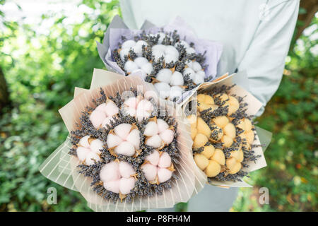 Trois belles et bouquets différents avec lavande en coton femme mains . fleurs couleur lilas. placé dans un sac de papier coloré de fleurs. mélange de couleurs. Banque D'Images