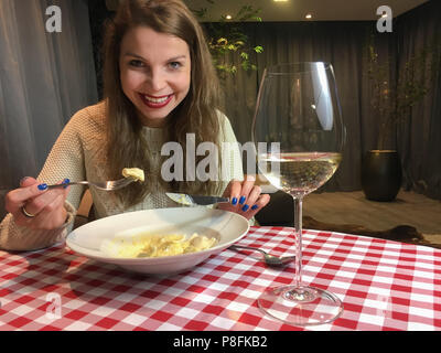Happy young woman eating pasta à la maison, regardant la caméra du mobile. Banque D'Images